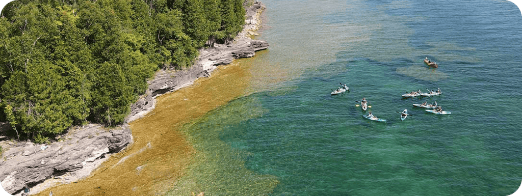 Kayakers paddling along the rocky cliffs of the Door County shoreline