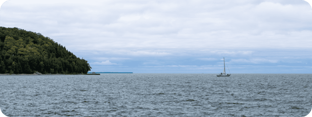 A sailboat on the bay near a wooded bluff